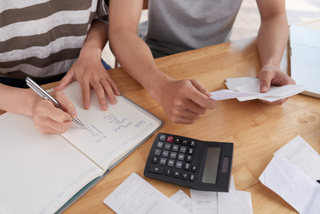 Duas pessoas analisando contas e despesas, caculadora sobre a mesa