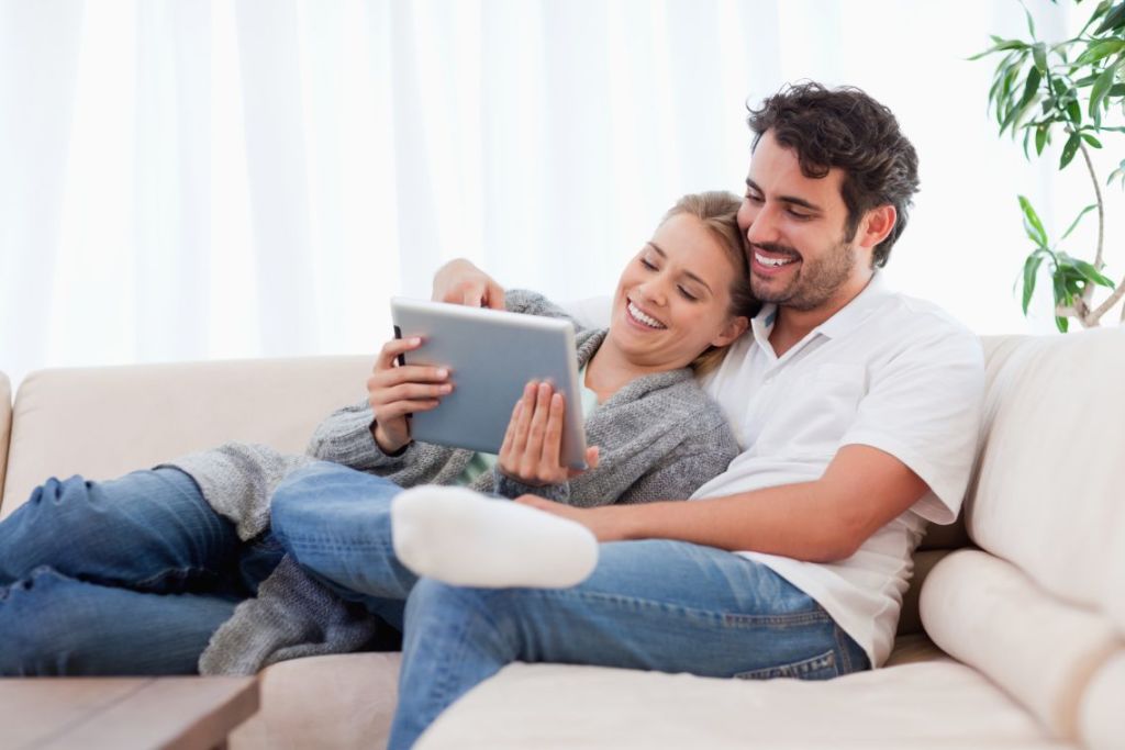 Casal no sofá sorrindo olhando para o laptop