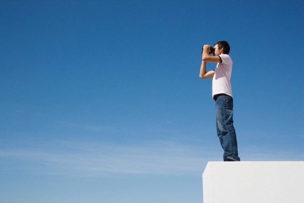 Home olhando por binóculos contra o céu azul