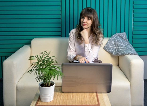 jovem sentada, computador, sofá, planta