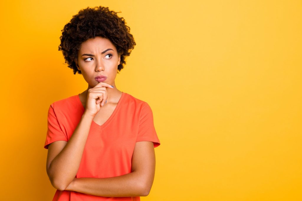 Mulher com mão no queixo pensando fundo amarelo